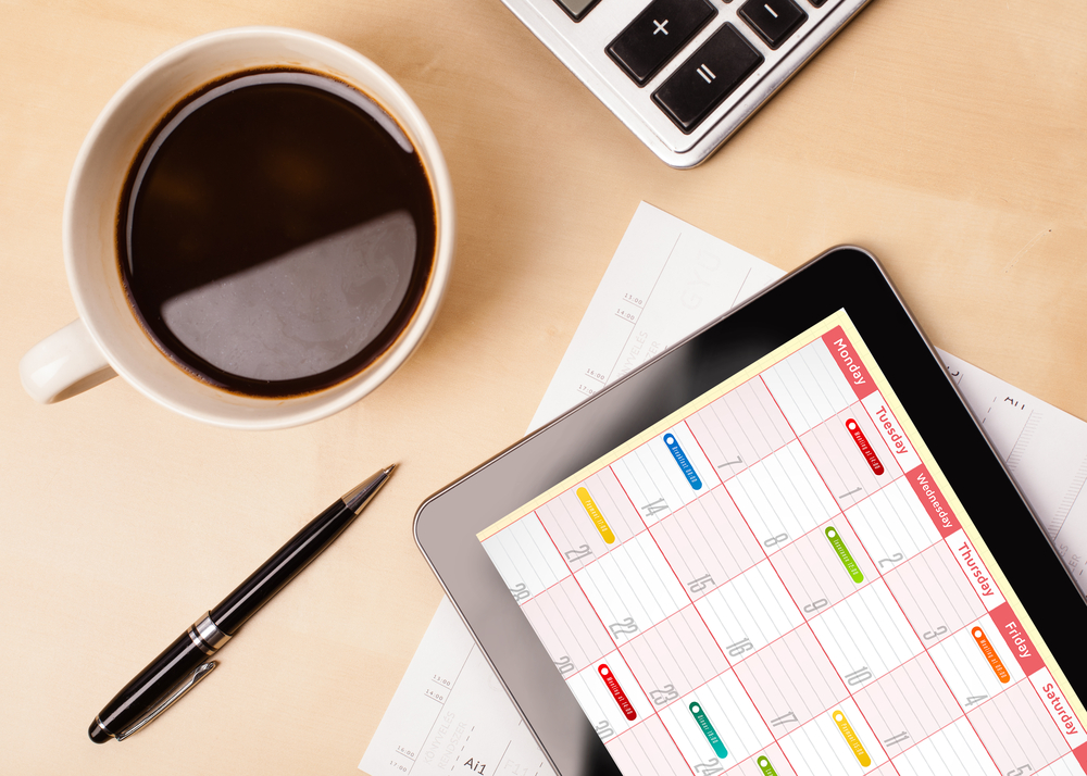 Workplace with tablet pc showing calendar and a cup of coffee on a wooden work table close-up-3